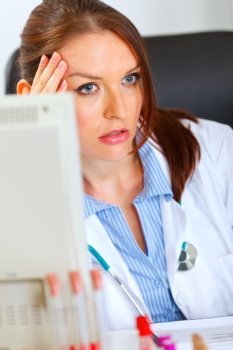 Concerned female doctor sitting at office table and holding hand near head
