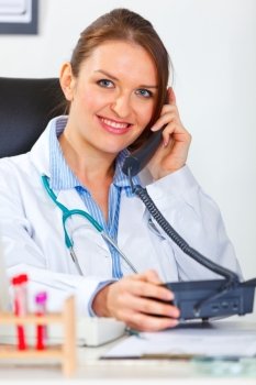 Smiling doctor woman sitting in office and speaking phone

