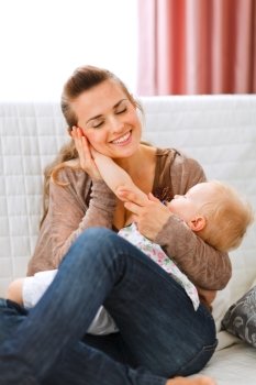 Young woman enjoying of being mother put baby’s hand to her cheek 
