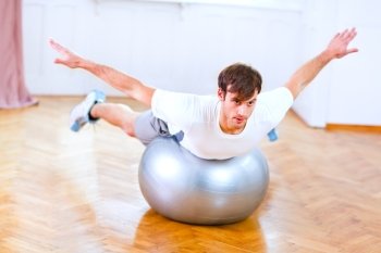 Healthy man making exercises on fitness ball
