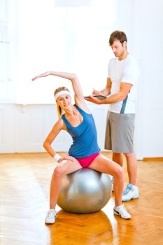 Smiling girl making exercises on fitness ball under the supervision of personal trainer 
