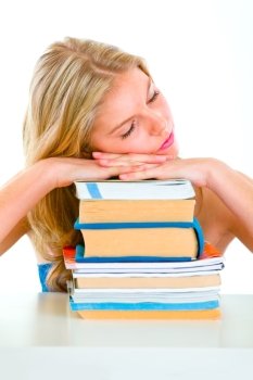 Tired young girl sitting at desk and sleeping on piles of books
