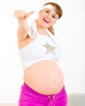 Smiling  pregnant woman in sportswear showing thumbs up gesture
