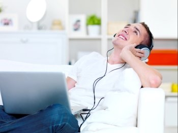 happy guy listening music in headphone from laptop and lying on the sofa