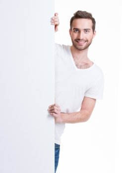 Happy young man look out from blank banner - isolated on white.