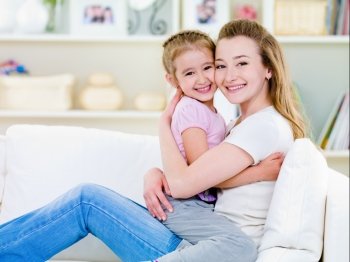 Happiness of mother with little daughter sitting together in embrase on the sofa - indoors
