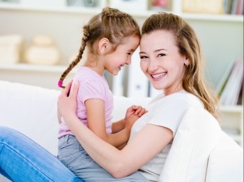 Portrait of happy smiling young woman with her little pretty daughter  -  indoors