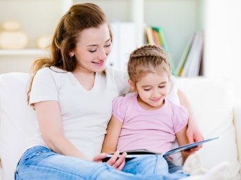 Mother with her little pretty daughter reading a book at home