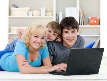 Smiling happy family with son lying together and using laptop at home - indoors
