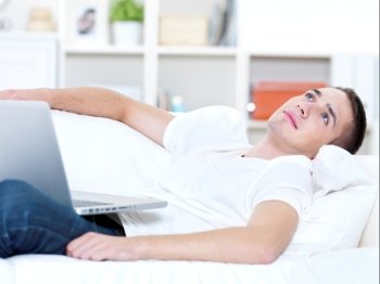young guy with laptop look outside on the sofa