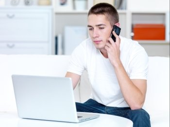 young man speaks on the phone and works on the laptop