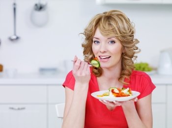 Young smiling woman eating salad in the kitchen - indoors