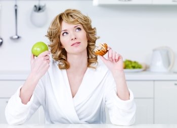 Thinking beautiful woman choosing between healthy food and caloric food - indoors