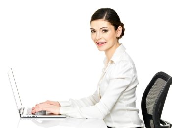 Beautiful smiling woman sits from the  table and working on laptop in white shirt - isolated on white. 
