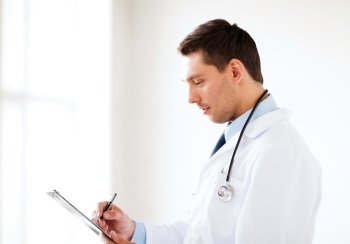healthcare and medical concept - male doctor with stethoscope writing prescription