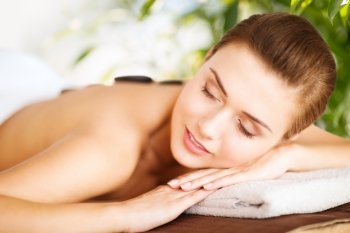 beauty and holidays concept - woman in spa salon with hot stones