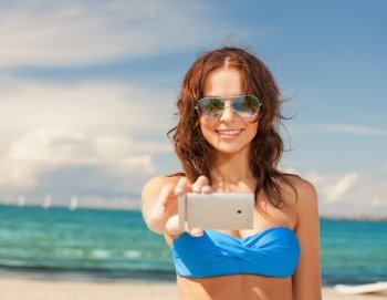 holidays and beach concept - beautiful woman in bikini and sunglasses with smartphone