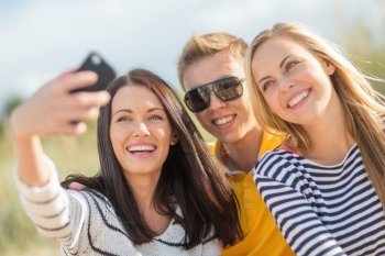 summer, holidays, vacation, happy people concept - group of friends taking photo picture with smartphone