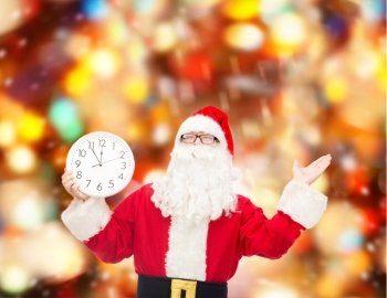 christmas, holidays and people concept - man in costume of santa claus with clock showing twelve over red lights background