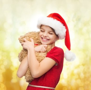 christmas, x-mas, winter, happiness concept - smiling girl in santa helper hat with teddy bear