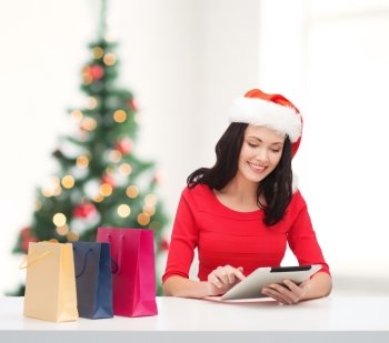 christmas, x-mas, online shopping concept - smiling woman in santa helper hat with shopping bags and tablet pc computer