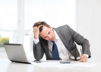 business, office, school and education concept - stressed businessman with laptop computer, papers and calculator