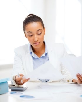 business and tax concept - african businesswoman working with calculator in office