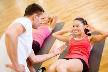 fitness, sport, training, gym and lifestyle concept - group of smiling women with male trainer doing sit ups on mats in the gym