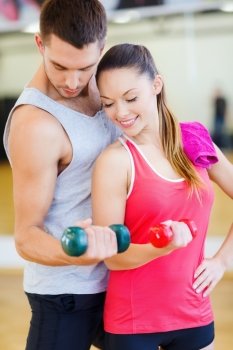 fitness, sport, training, gym and lifestyle concept - two smiling people working out with dumbbells in the gym
