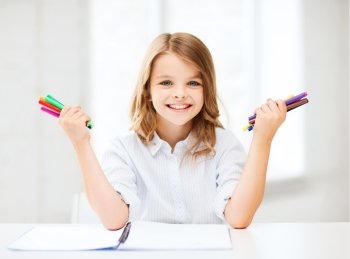 education, creation and school concept - smiling little student girl showing colorful felt-tip pens at school