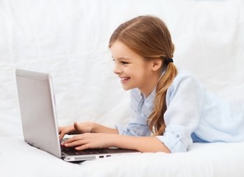 home, leisure, technology and internet concept - little student girl with laptop computer at home