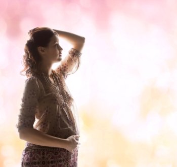 family, motherhood and pregnancy concept - silhouette backlight picture of pregnant beautiful woman touching her tummy