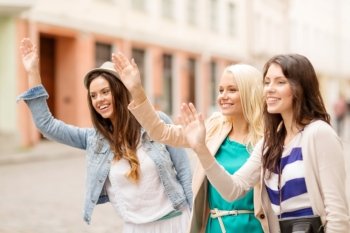 holidays and tourism concept - three beautiful girls waving hands in the city