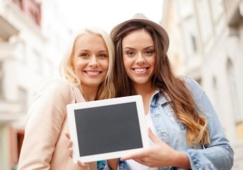 holidays, advertisement, technology and tourism concept - two beautiful girls toursits with blank screen tablet pc in the city