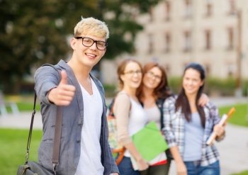 summer holidays, education, campus and teenage concept - smiling male student in black eyeglasses with group in the back showing thumbs up