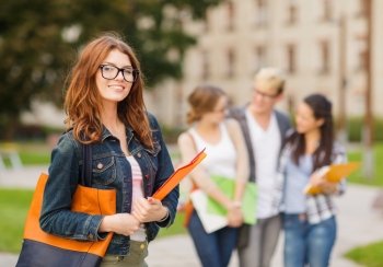 summer holidays, education, campus and teenage concept - smiling female student in black eyeglasses with folders and group in the back