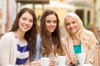 holidays, food and tourism concept - three beautiful girls drinking coffee in cafe