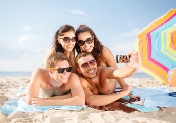 summer, holidays, vacation, technology and happiness concept - group of smiling people in sunglasses taking picture with smartphone on beach