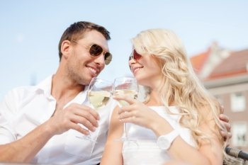 summer holidays and dating concept - smiling couple in sunglasses drinking wine in cafe