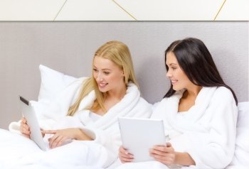 hotel, travel, friendship, internet, technology and happiness concept - smiling girlfriends with tablet pc computers in bed