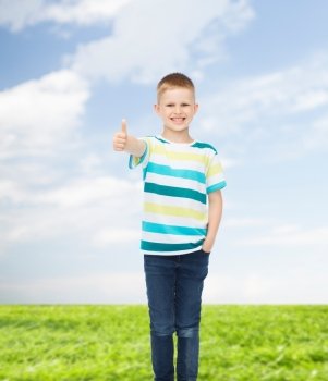 happiness, childhood, environment and people concept - smiling little boy in casual clothes showing thumbs up over natural background