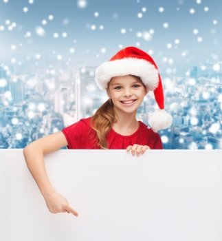 christmas, holidays, people, advertisement and sale concept - happy little girl in santa helper hat with blank white board over snowy city background