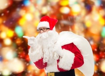 christmas, holidays and people concept - man in costume of santa claus with bag pointing finger over red lights background