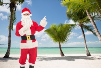 christmas, holidays, gesture and people concept - man in costume of santa claus pointing fingers over tropical beach background