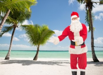 christmas, holidays, gesture and people concept - man in costume of santa claus over tropical beach background