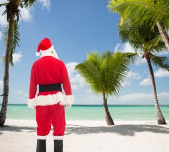 christmas, holidays and people concept - man in costume of santa claus from back over tropical beach background
