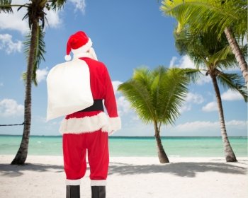 christmas, holidays and people concept - man in costume of santa claus with bag from back over tropical beach background
