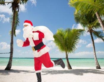christmas, holidays and people concept - man in costume of santa claus running with bag over tropical beach background