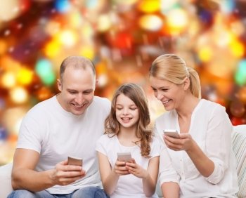 family, holidays, technology and people - smiling mother, father and little girl with smartphones over red lights background