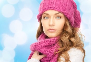 happiness, winter holidays, christmas and people concept - close up of young woman in pink hat and scarf over blue lights background
